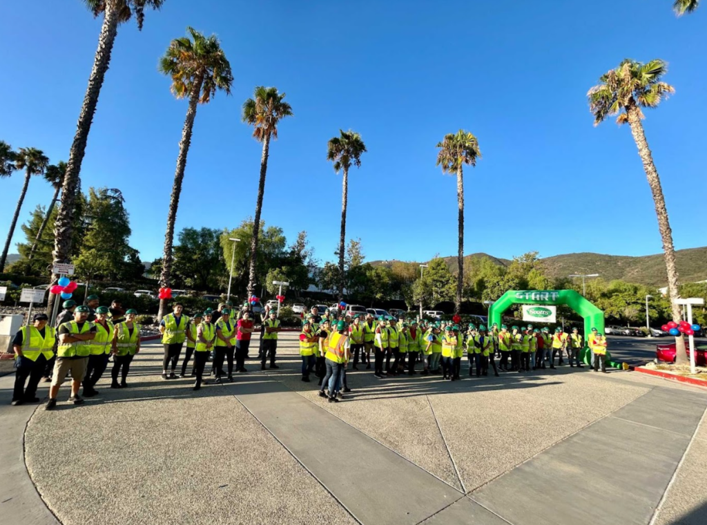 Large group of people near the finish line for a walk, with palm trees in the background